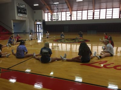 The cheerleaders stretch as a team before they begin tryouts.
