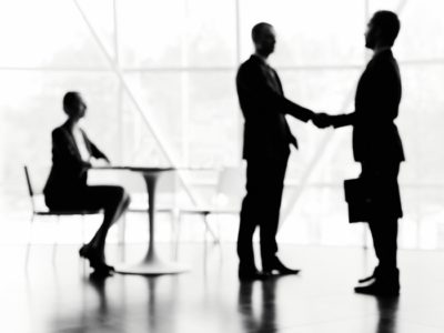 Blurred image of student looking at two businessmen handshaking in office